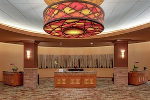 A lobby with a reception desk, a decorative ceiling light, and a wall with vertical patterns. - Embassy Suites by Hilton Loveland Conference Center (Loveland)