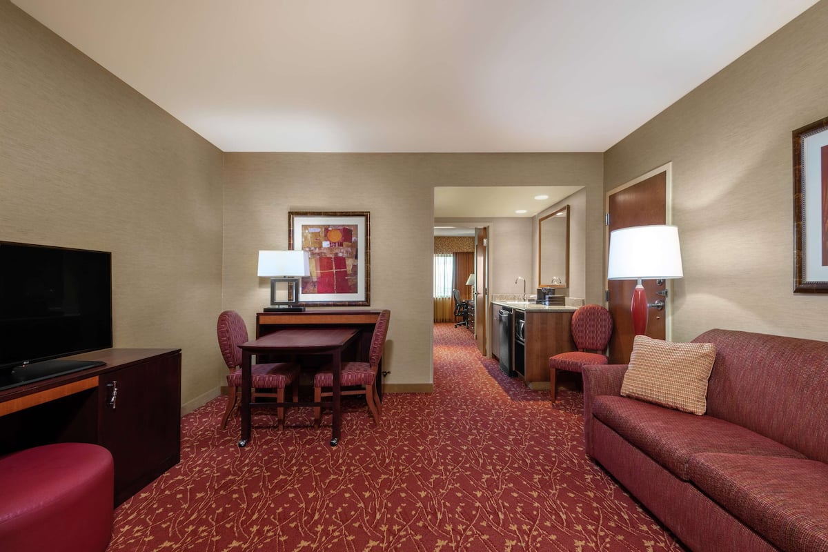 A hotel room with a television, a dining table with chairs, a sofa, and a kitchen area.