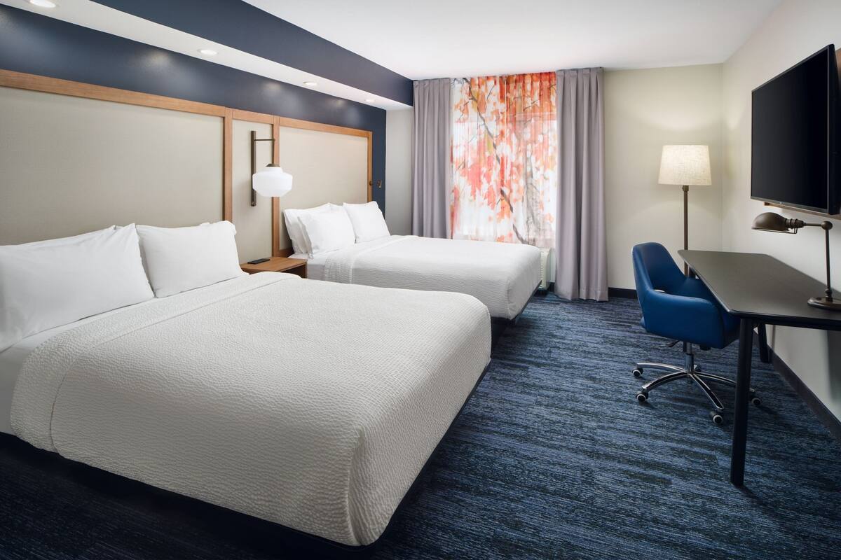 Een hotelkamer met twee bedden, een bureau, een stoel, een televisie en een raam met gordijnen.