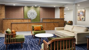 A modern lobby with a reception desk, green and brown upholstered chairs, a round white table, and a beige sofa. - Fairfield Inn & Suites by Marriott Auburn Opelika (Opelika)