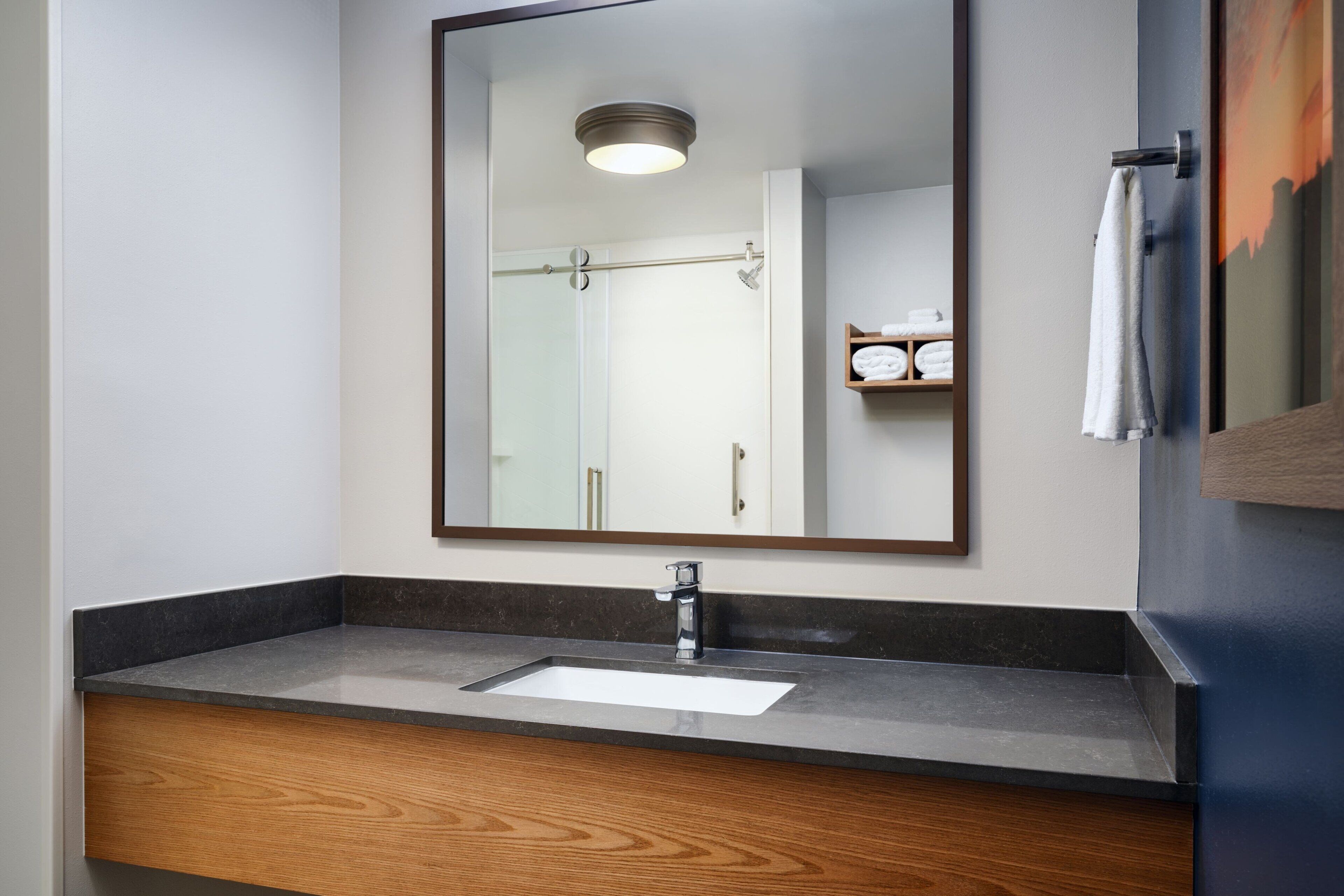 A bathroom with a large mirror, a sink, and a towel rack.