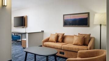 A hotel room with a sofa, a small table, a TV, a desk, and a lamp.