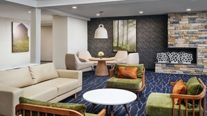 A modern lounge area with a sofa, armchairs, a round table, and a fireplace. - Fairfield Inn & Suites by Marriott Auburn Opelika (Opelika)