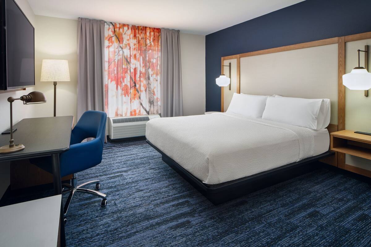 Een hotelkamer met een bed, bureau, stoel en een groot raam met gordijnen.