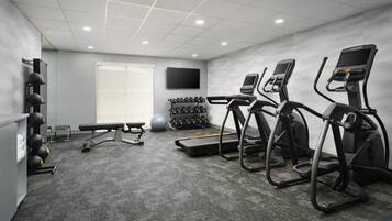 A gym with treadmills, a bench, dumbbells, and a TV on the wall.