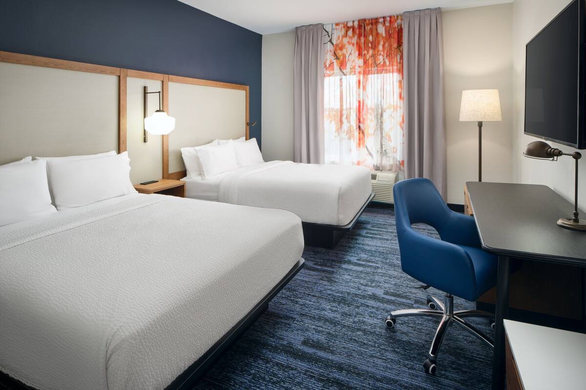 Een hotelkamer met twee bedden, een bureau, een stoel, een lamp en een televisie.