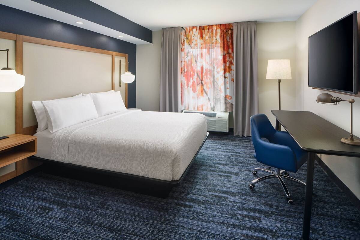 Een hotelkamer met een bed, bureau, stoel, televisie en gordijnen.