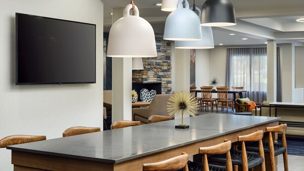 A modern hotel dining area with a long table, wooden chairs, and pendant lighting. - Fairfield Inn & Suites by Marriott Auburn Opelika (Opelika)