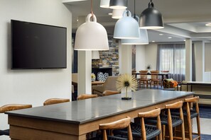 Uma área de jantar de hotel moderna, com uma mesa comprida, cadeiras de madeira e iluminação pendente.