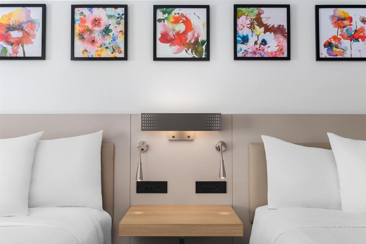 A hotel room with two beds, a bedside table, and four framed floral artworks on the wall.