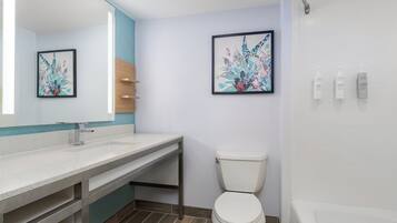 A modern bathroom with a white sink, a toilet, and a bathtub. There are two framed artworks on the wall.