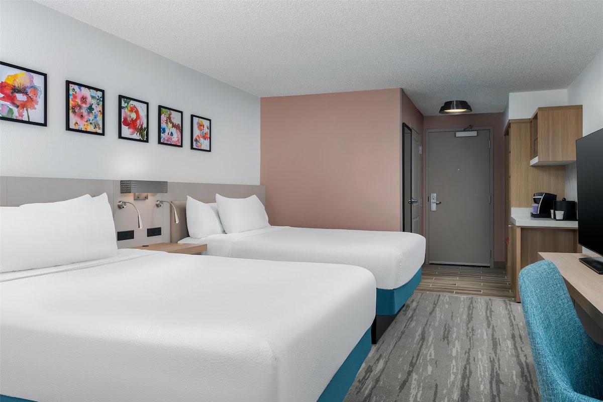 A hotel room with two beds, a desk, a TV, and a door to the bathroom.