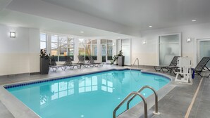 An indoor swimming pool with clear blue water, surrounded by lounge chairs and potted plants.