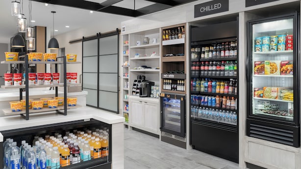 A modern grocery store with refrigerated sections for chilled and frozen items, shelves stocked with beverages, and a coffee machine.