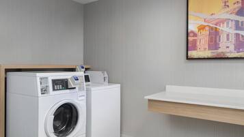A modern laundry room with a front-loading washing machine and dryer, a wooden shelf above the dryer, and a white countertop.