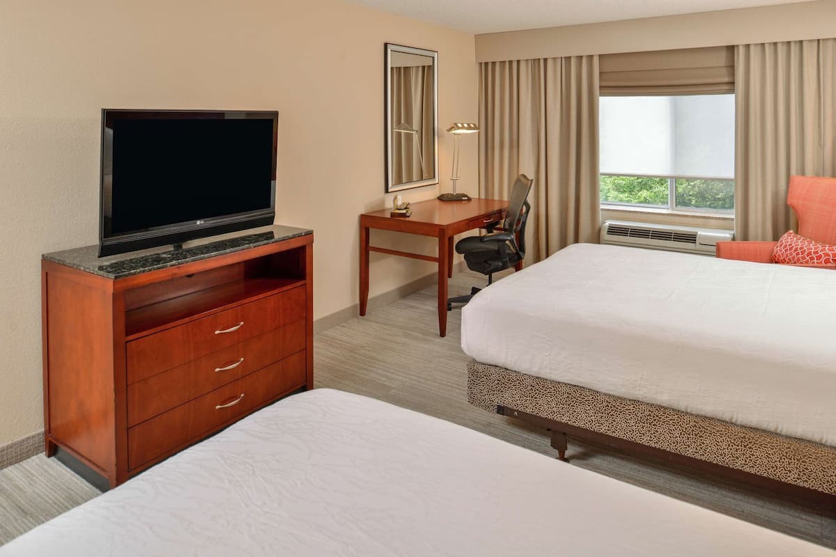A hotel room with a bed, a desk with a chair, a television, a mirror, and a window with curtains.