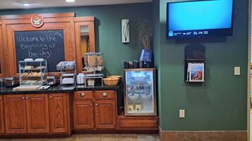 A breakfast bar with wooden cabinets, a chalkboard sign, a coffee machine, and a TV displaying the weather.