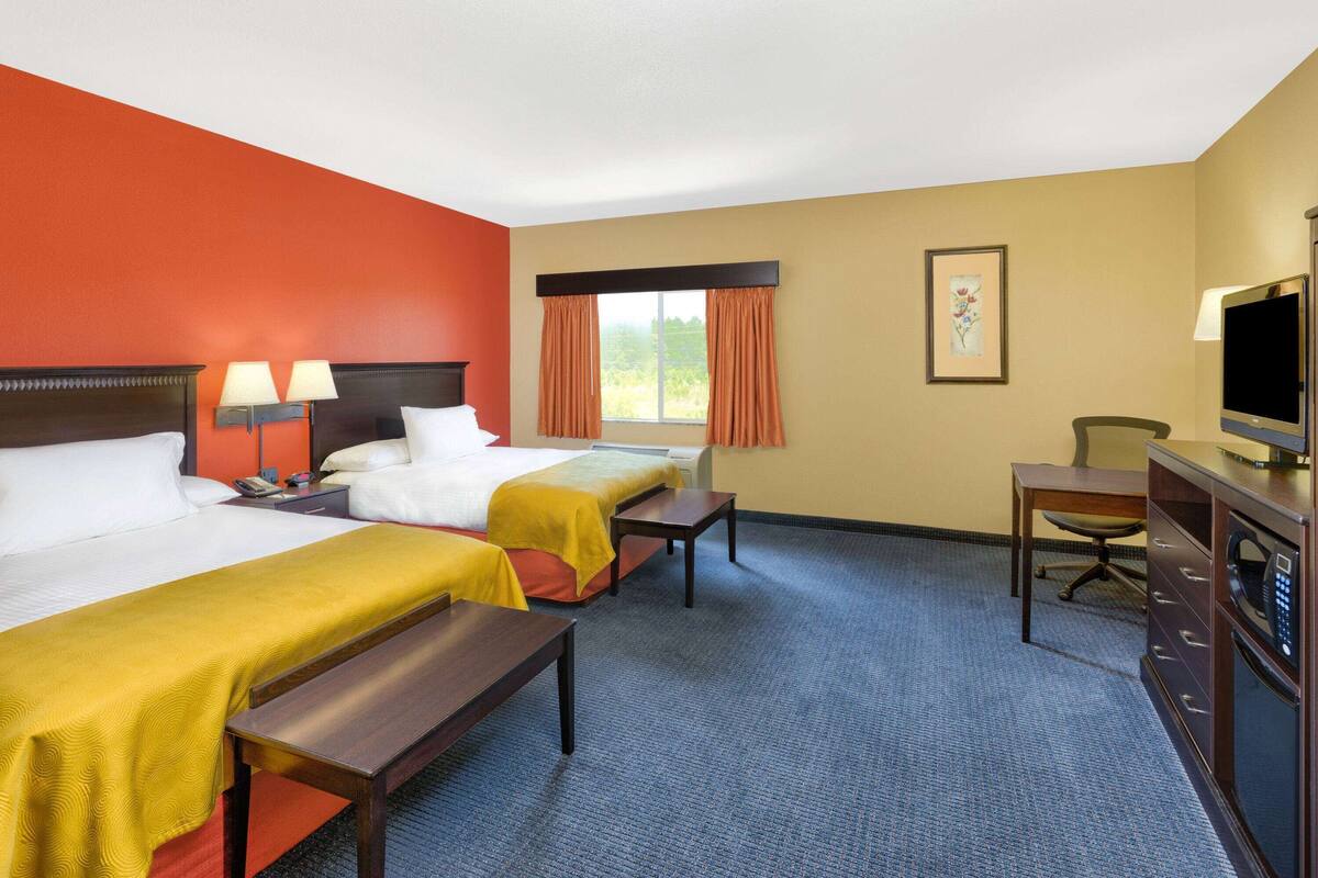 Habitación de hotel con dos camas, un escritorio, una silla, un televisor y una ventana con cortinas.