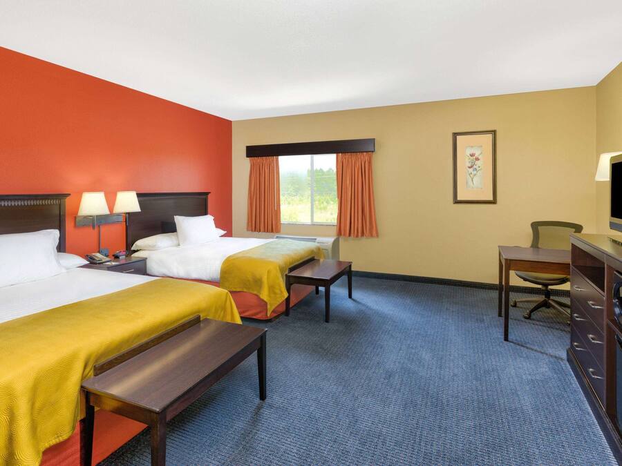 A hotel room with two beds, a desk, a chair, a television, and a window with curtains.