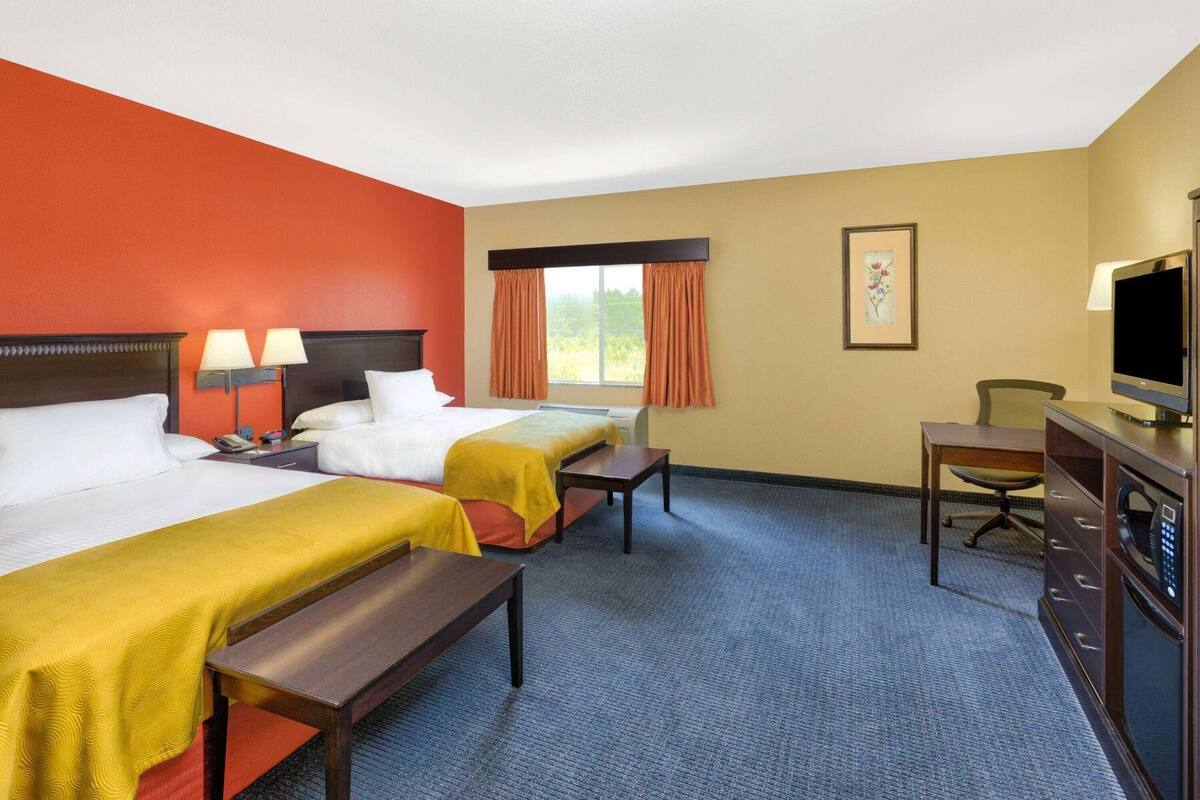 Habitación de hotel con dos camas, un escritorio, una silla, un televisor y una ventana con cortinas.