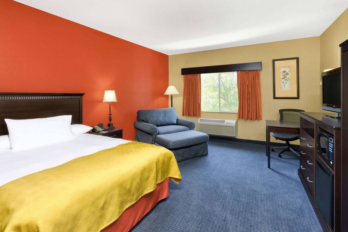 Una habitación de hotel con cama, escritorio con silla, televisor y ventana con cortinas.