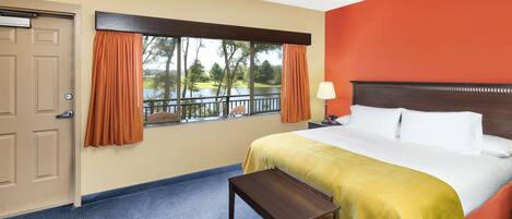 A hotel room with a bed, a nightstand, a lamp, a window with curtains, and a view of a lake.