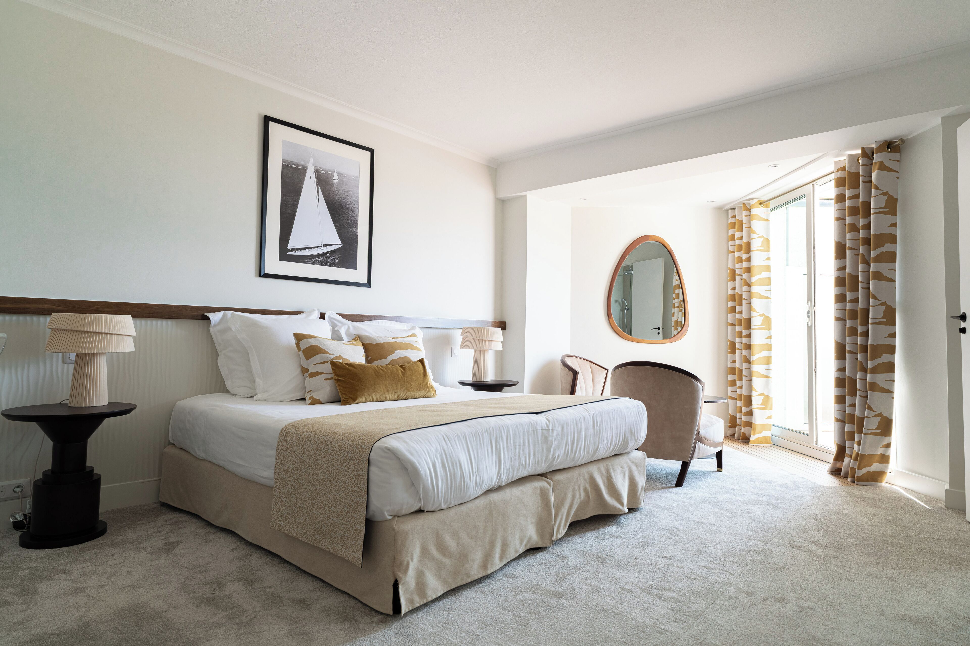Une chambre à coucher bien rangée, avec un lit, des tables de chevet, une chaise, un miroir et une porte avec des rideaux.
