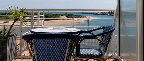 A balcony with a table and chairs overlooking a beach.