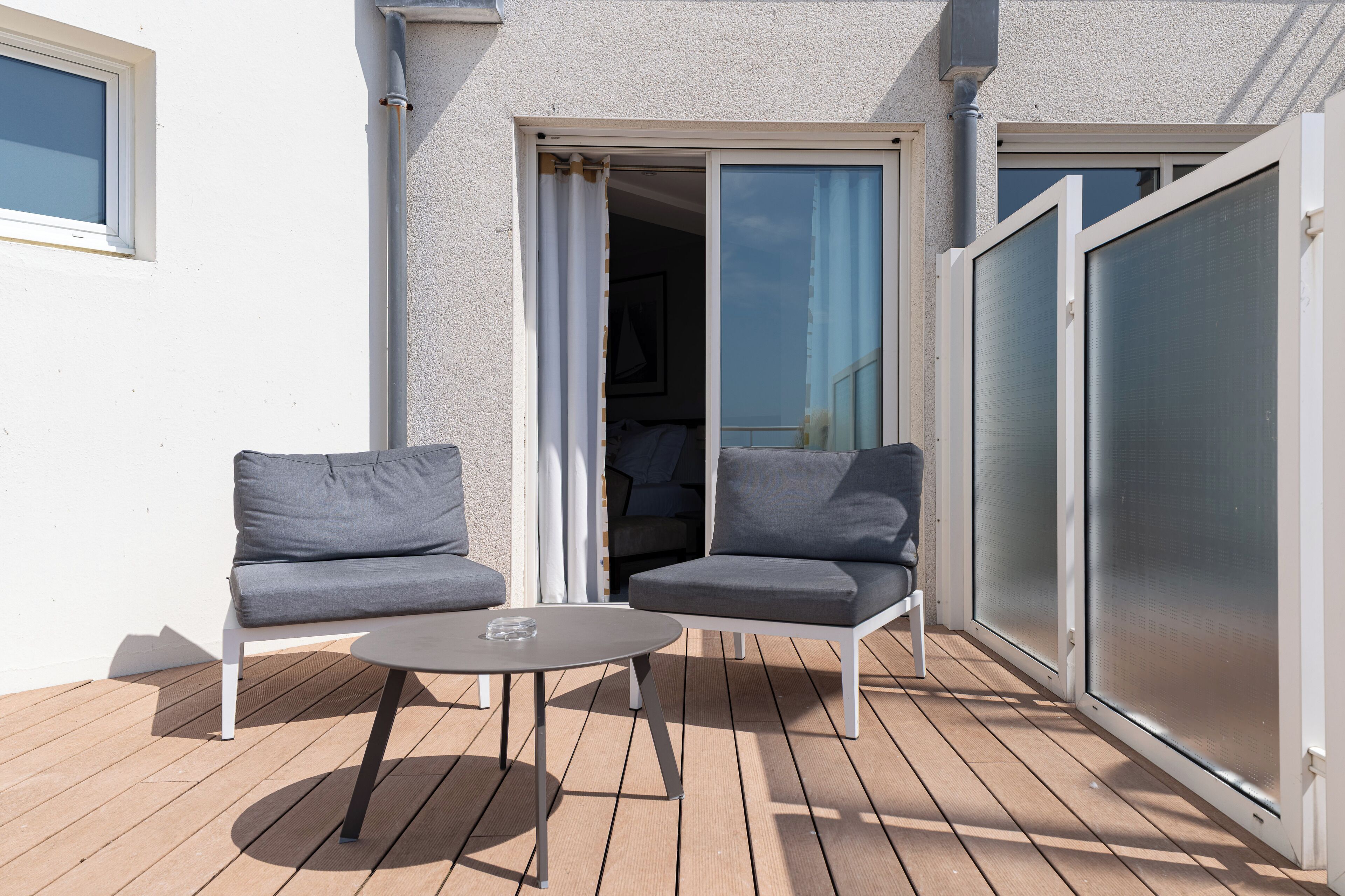 Ein Balkon mit zwei grauen Sitzgelegenheiten und einem kleinen runden Tisch.