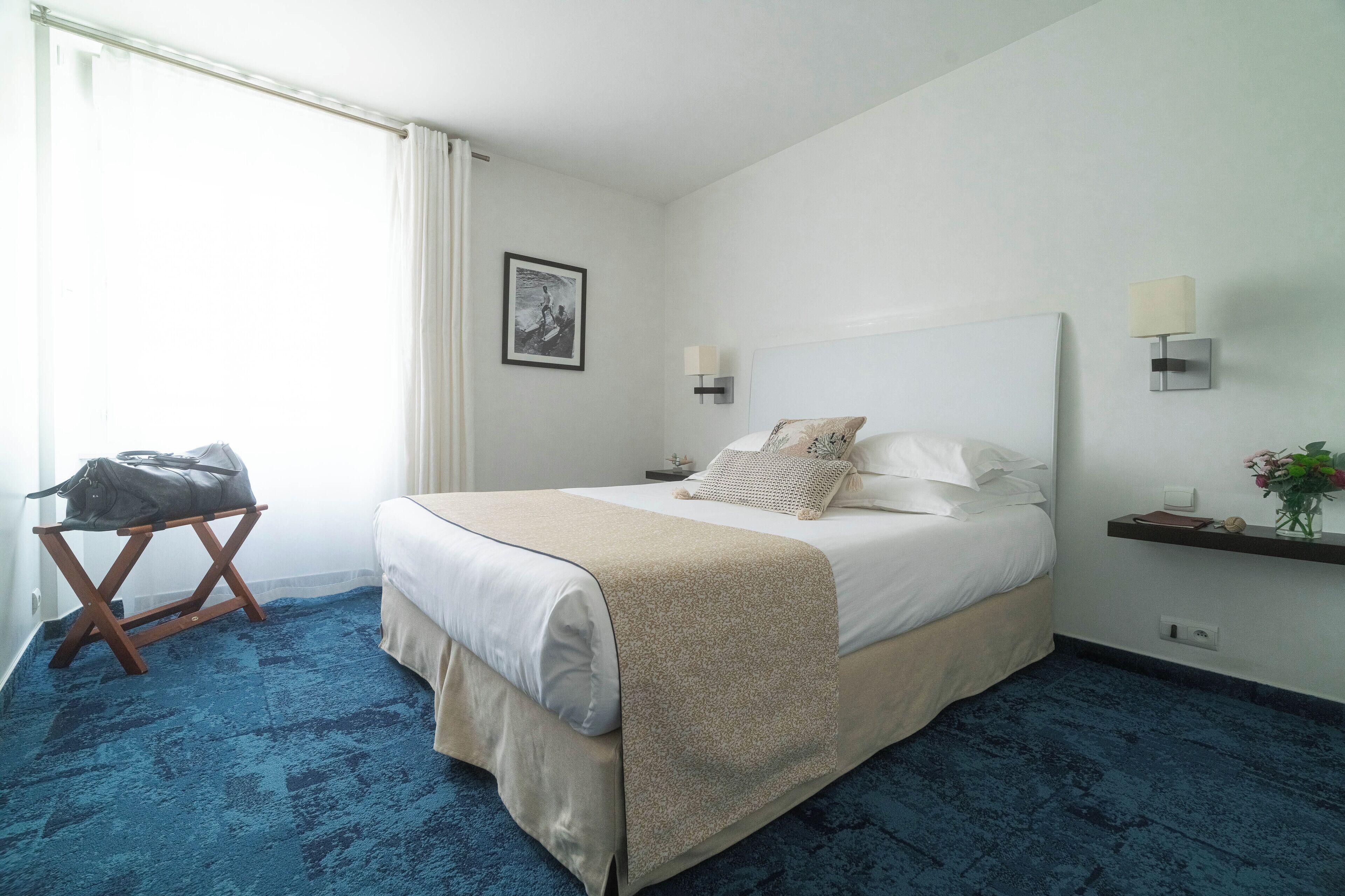 Habitación de hotel con una cama grande, una mesita con una bolsa, un cuadro en la pared y una mesita de noche con una lámpara.