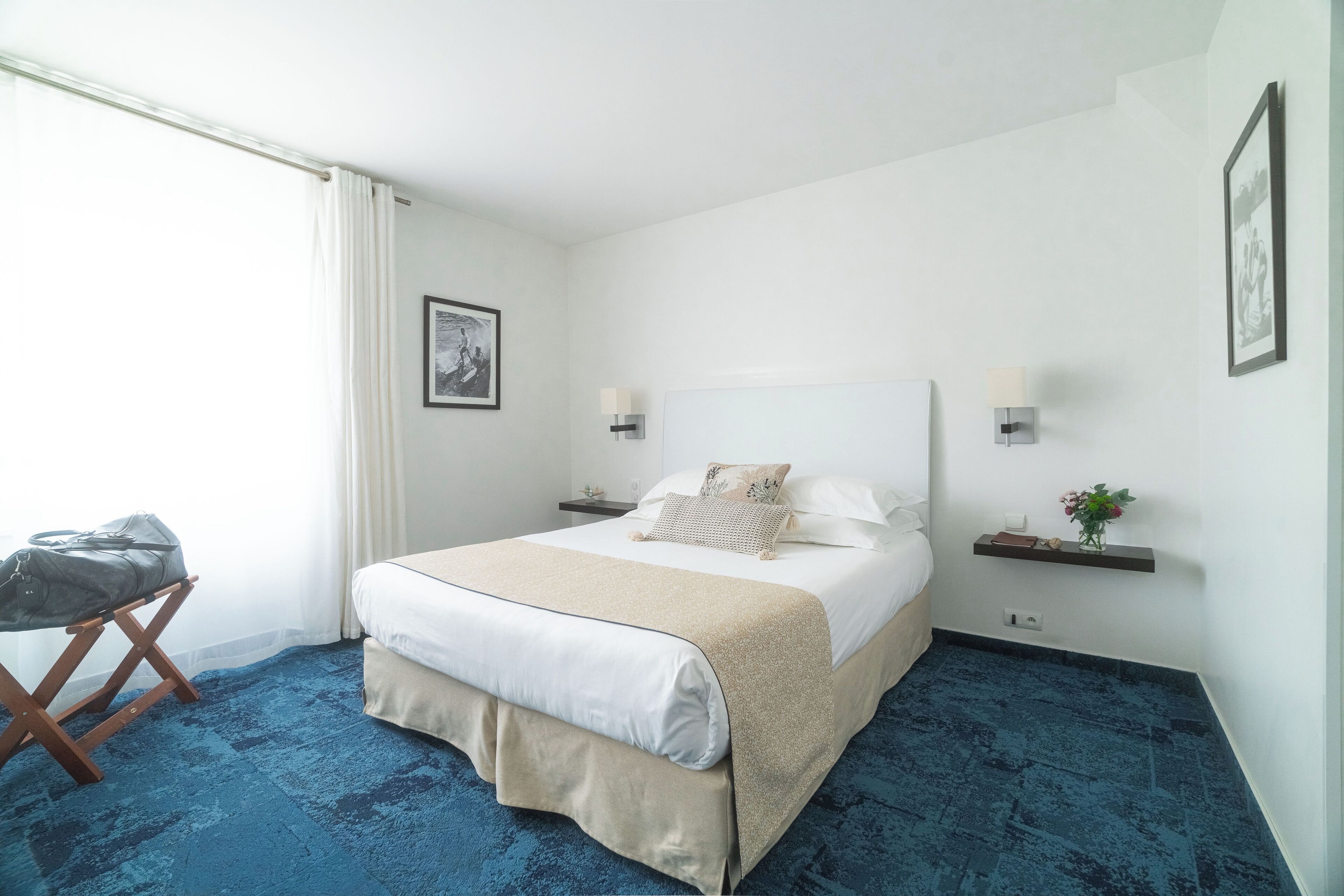 A hotel room with a large bed, a small table, a chair, and a window with curtains.