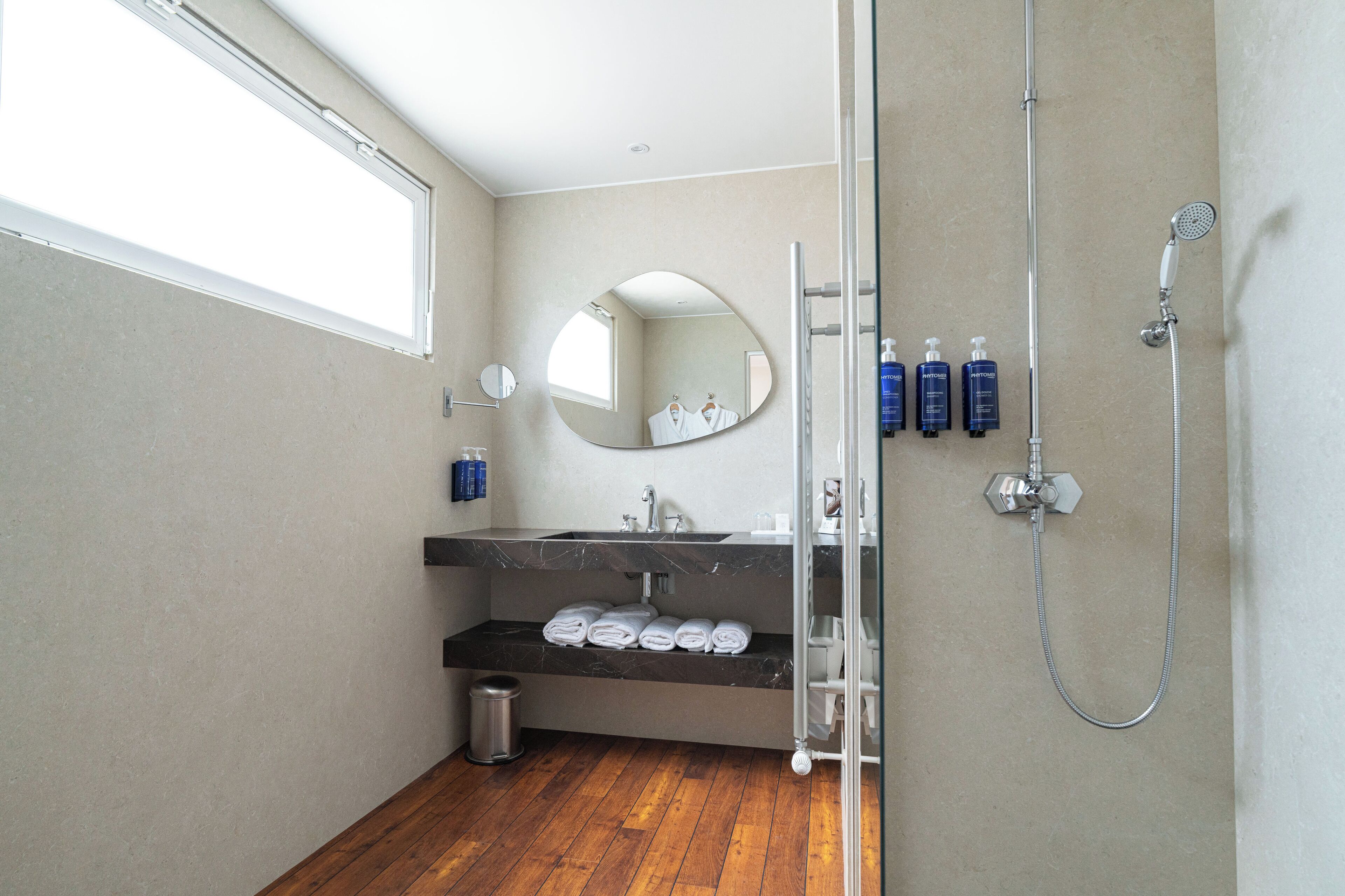 A modern bathroom with a large mirror, a shower, and a sink with neatly folded towels.