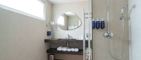 A modern bathroom with a large mirror, a shower, and a sink with neatly folded towels.