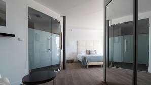 A modern hotel room with a glass partition, a bed with a white headboard, a small round table, and a chair. - La Marine (Barneville-Carteret)