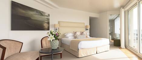 Une chambre d’hôtel avec un lit, une chaise, une petite table sur laquelle se trouve un vase, et une grande fenêtre.
