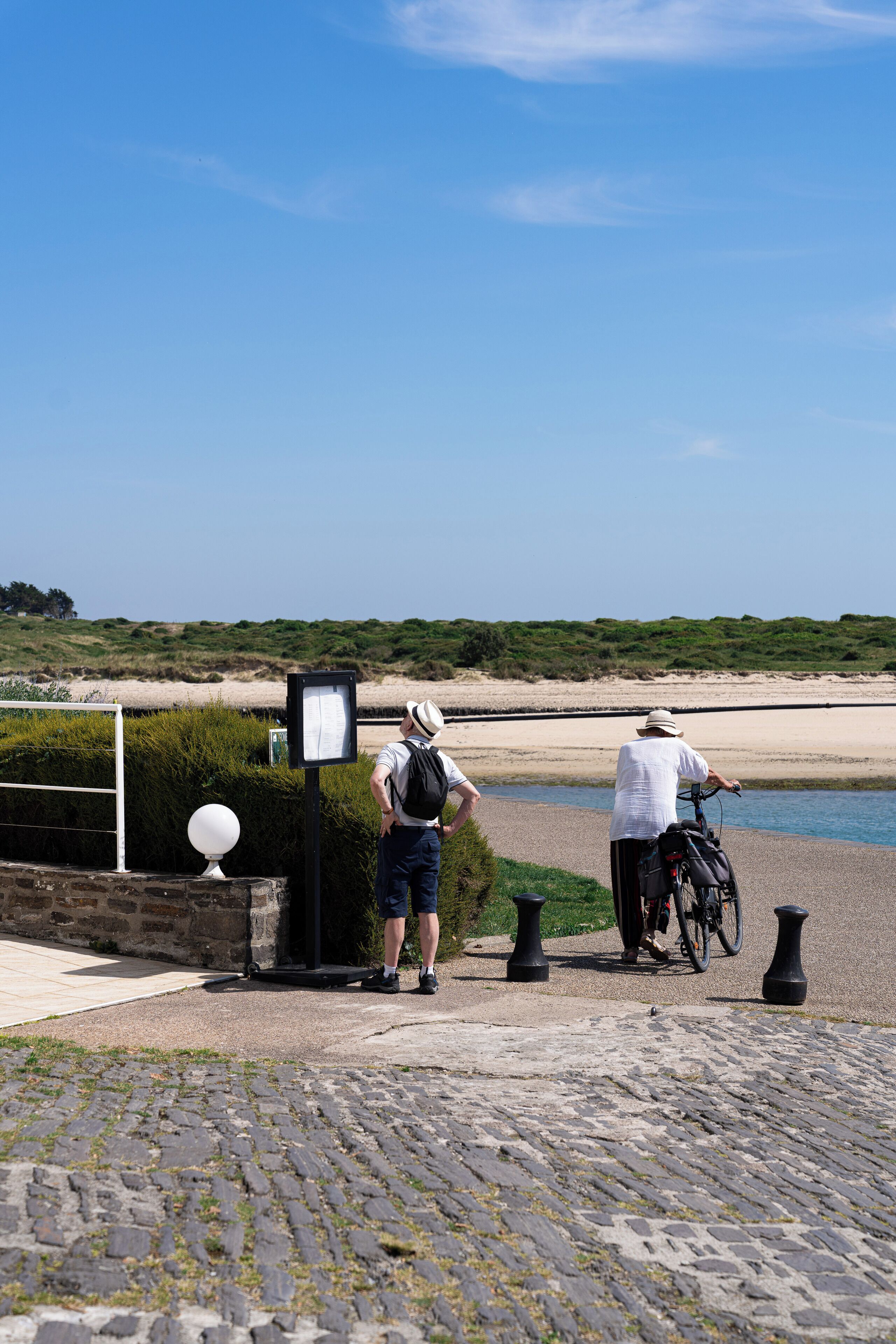 Un camino adoquinado que lleva a una playa, con un cartel y una bicicleta.