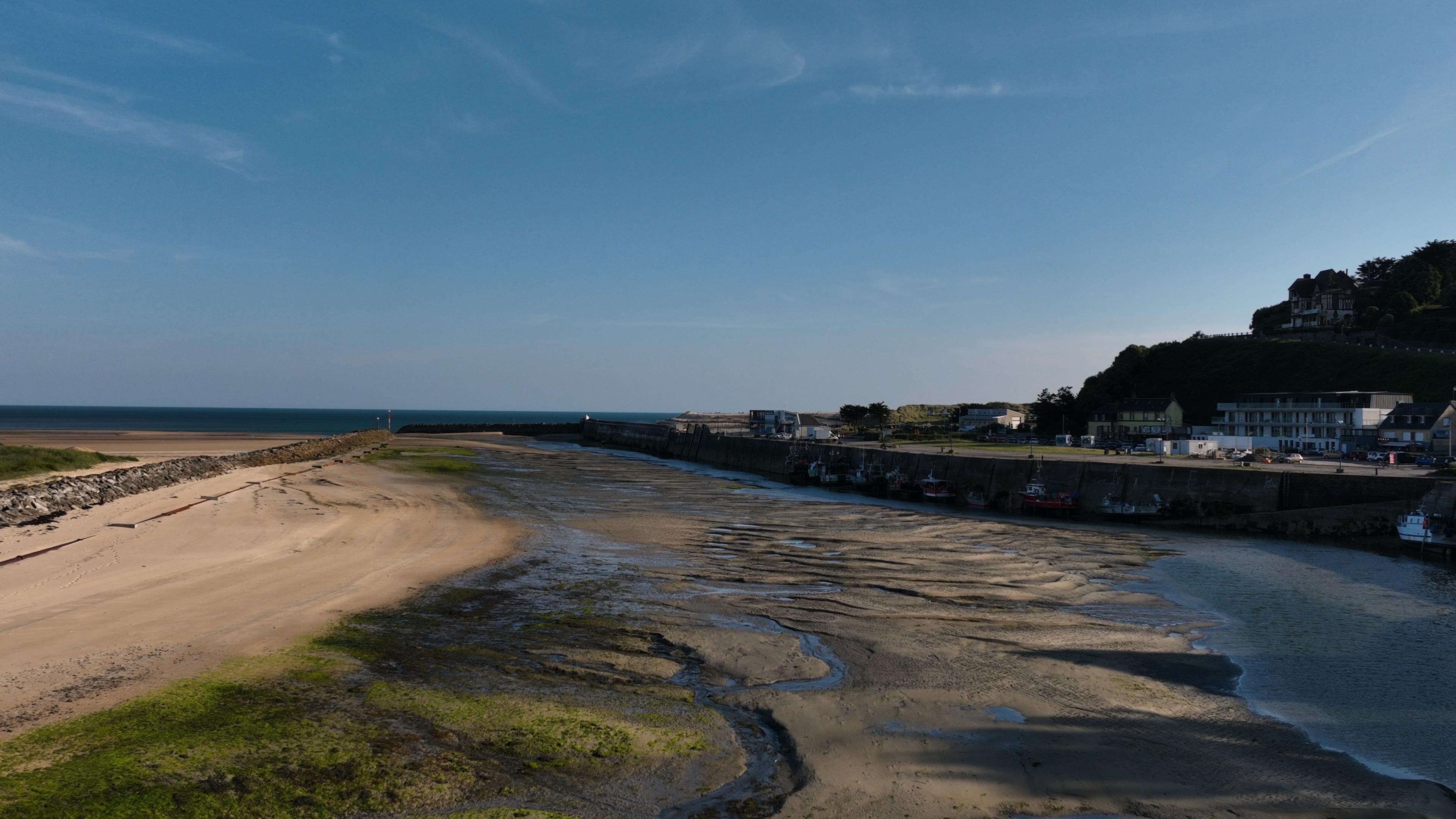A coastal area with a sandy beach, a rocky shoreline, and a row of buildings along the coast.