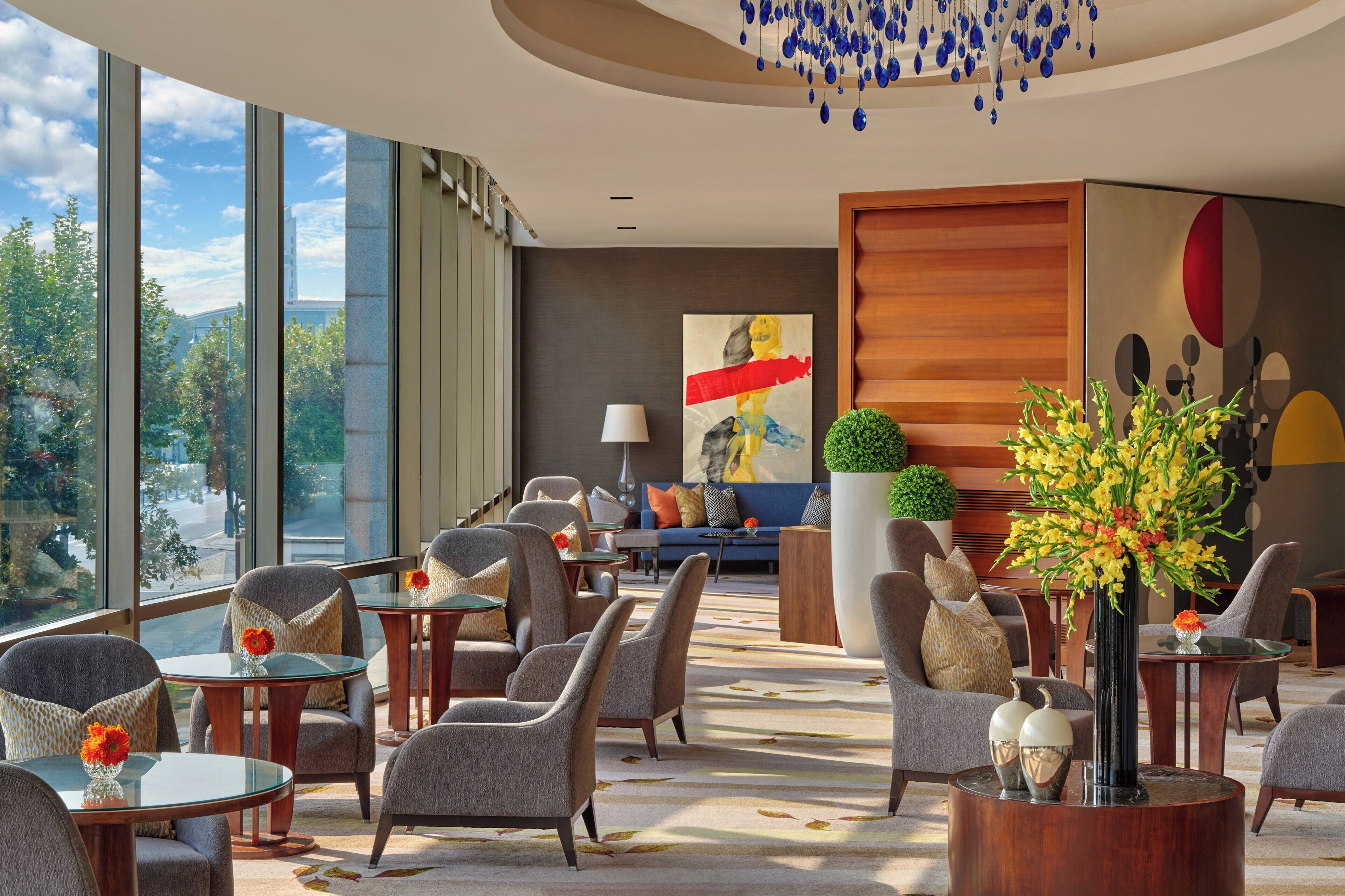 A hotel lobby with seating areas, a large window, and a modern chandelier.