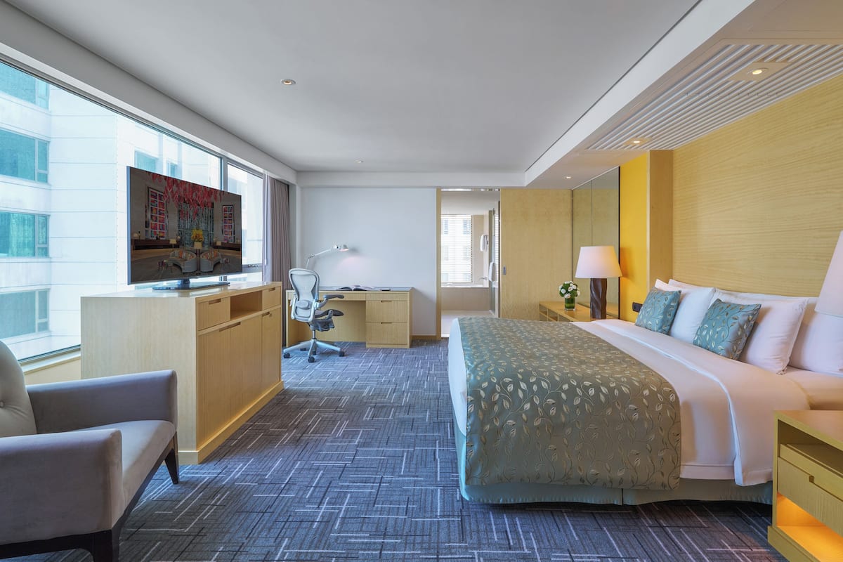 Een hotelkamer met een bed, bureau, stoel en een televisie aan de muur.