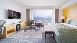 A hotel room with a bed, desk, chair, and a view of a city skyline. - Marco Polo Wuhan (Wuhan)