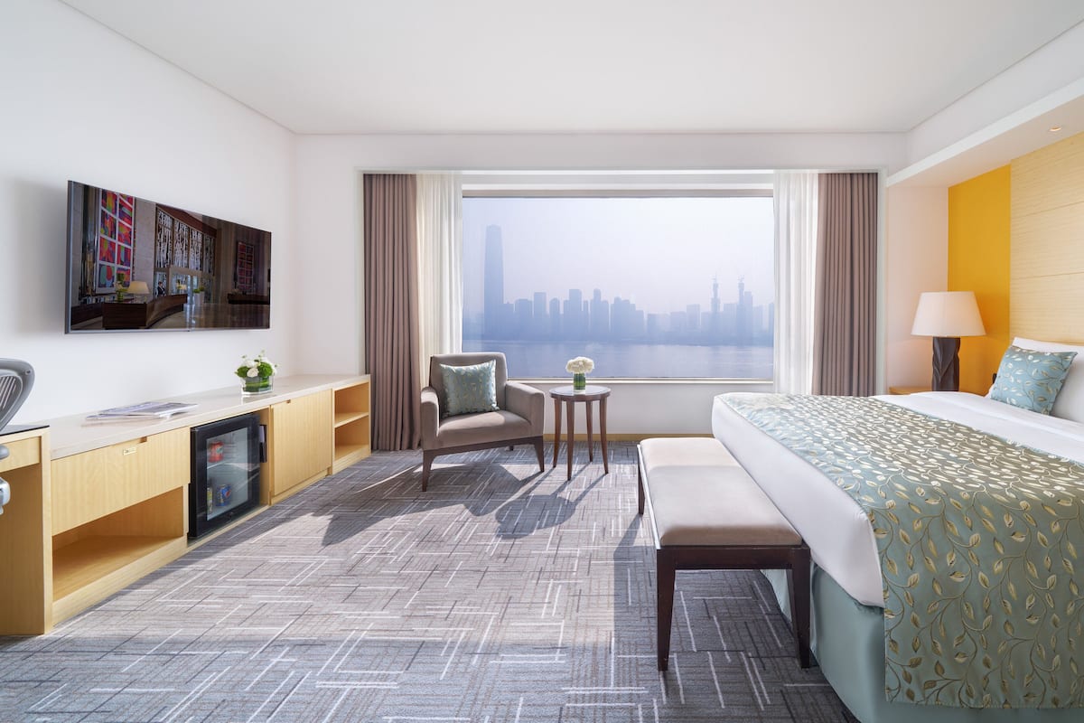Een hotelkamer met een bed, bureau, stoel en uitzicht op een stadsbeeld.
