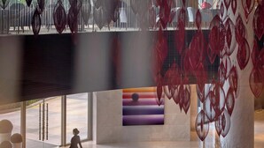 A spacious lobby with a modern design, featuring a large seating area with sofas and a coffee table, a decorative wall with a sunset painting, and hanging red glass ornaments. - Marco Polo Wuhan (Wuhan)