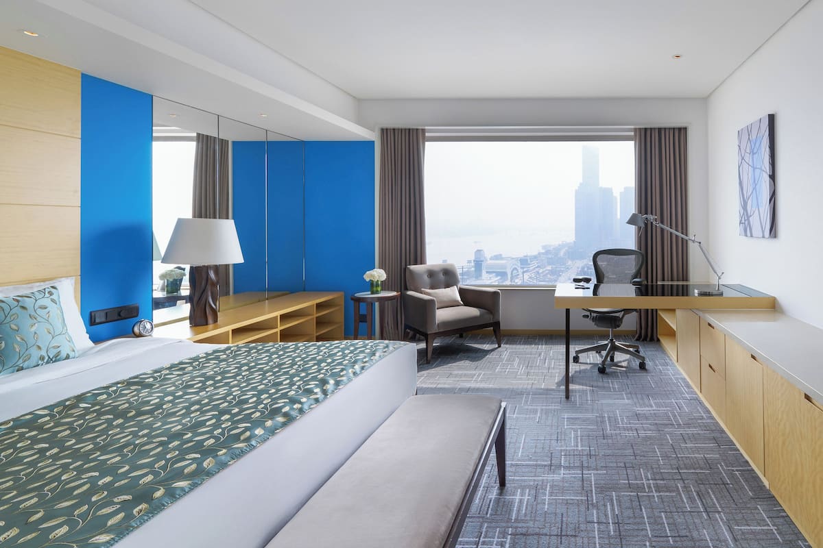 Een moderne hotelkamer met een bed, bureau, stoel en een groot raam met uitzicht op de stad.