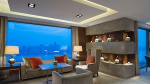 A modern hotel room with a large window offering a city view, a sofa with red cushions, a coffee table, and a decorative shelf with vases. - Marco Polo Wuhan (Wuhan)