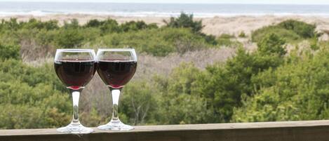 Two wine glasses on a balcony overlooking a beach with a view of the ocean and greenery.