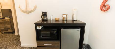 A kitchenette with a microwave, refrigerator, coffee maker, and a trash bin.