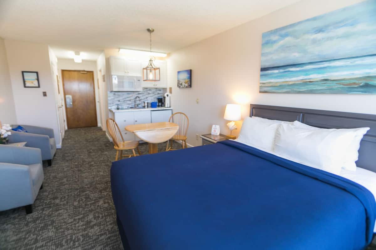 Habitación de hotel con cama, escritorio, silla, lámpara y un cuadro en la pared.