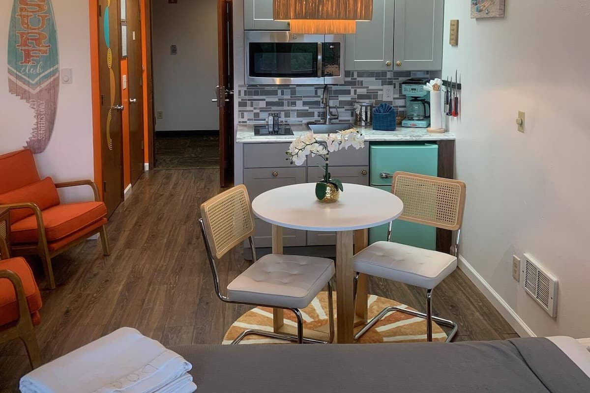 Un espacio habitable compacto con kitchenette, un comedor con una mesa redonda y sillas, y una cama con un edredón blanco impecable.