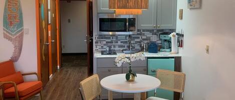 A compact living space with a kitchenette, a dining area with a round table and chairs, and a bed with a neatly folded white blanket.