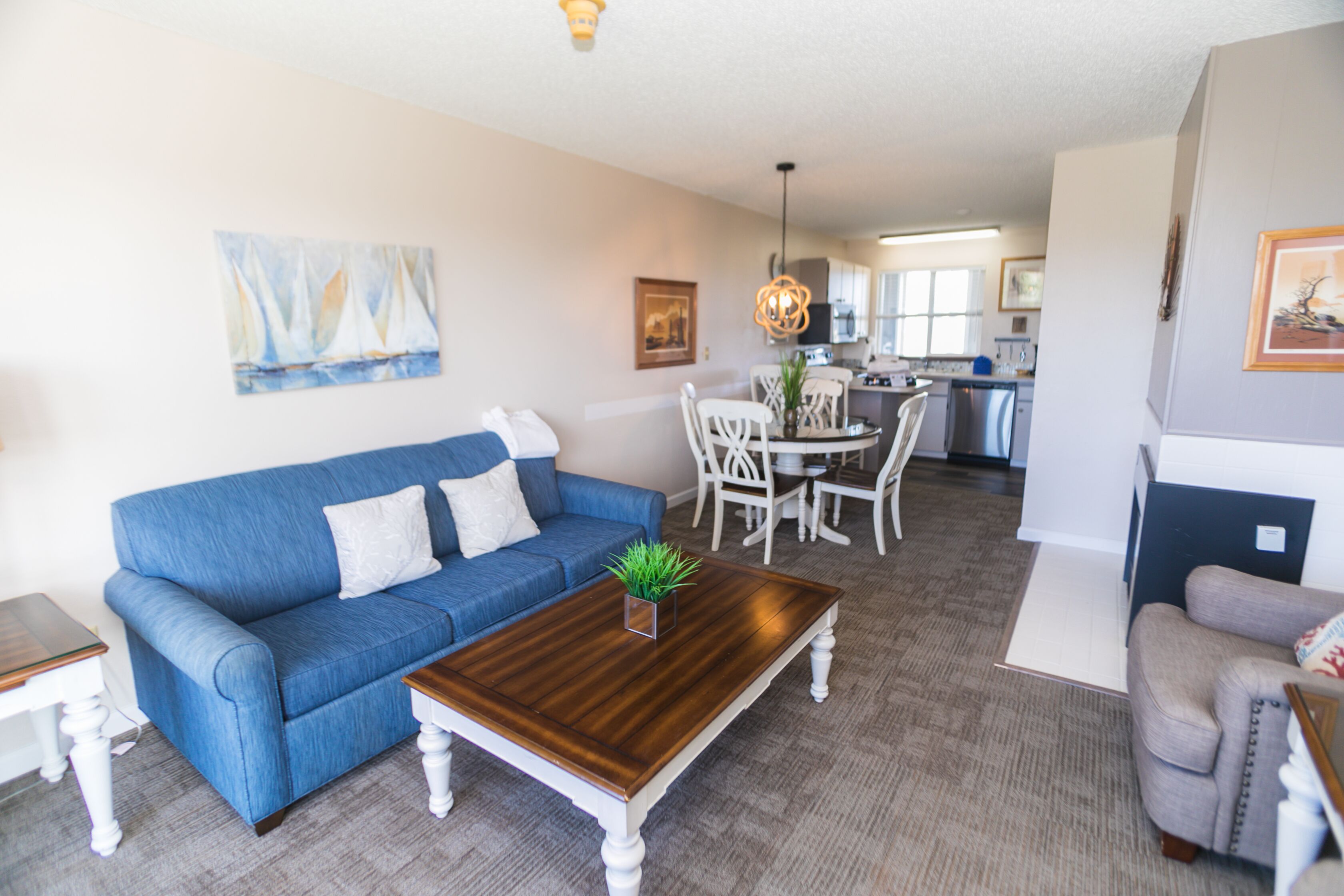 A living room with a blue sofa, a wooden coffee table, and a dining area with white chairs.